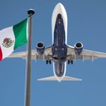 Bottom View of Passenger Airplane Flying Over Waving Mexico Flag On Pole.