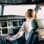 Woman pilot sitting in airplane cockpit, wearing headset.