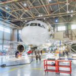 Aircraft inside the aviation hangar, maintenance service. Airplane technician worker working around. Bright light outside the gate.