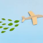 Wooden airplane model emitting fresh green leaves on blue backgr
