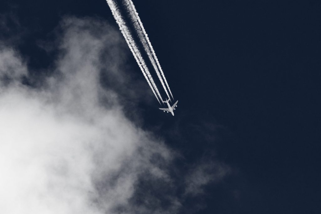 Flying airplane leaving contrails in the blue sky with clouds.