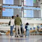 Rear,View,Of,African,Family,With,Luggage,Looking,At,Scheduled