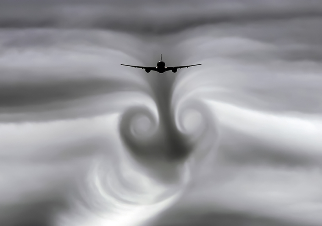 A commercial aircraft flies through cloudy skies, creating dramatic wake vortices that spiral behind it in the turbulent air.