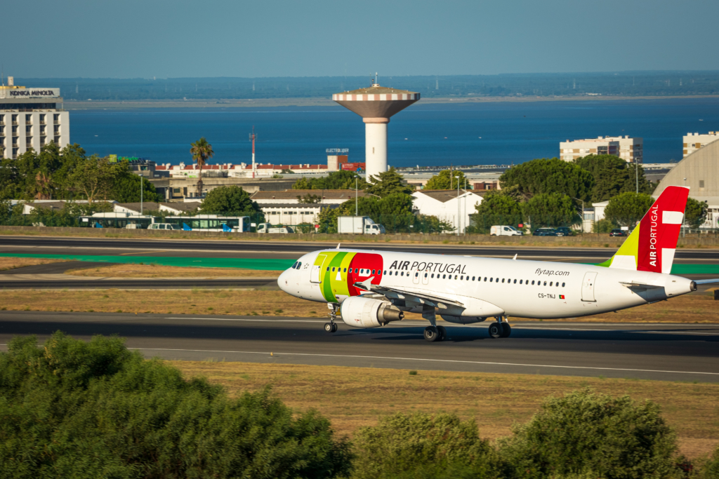 Jul 23, 2023 - Lisbon, Portugal. Air Portugal or TAP airplane on runway of Humberto Delgado airport, known as Lisbon airport, on sunny day. Residential area and river Tagus in background.