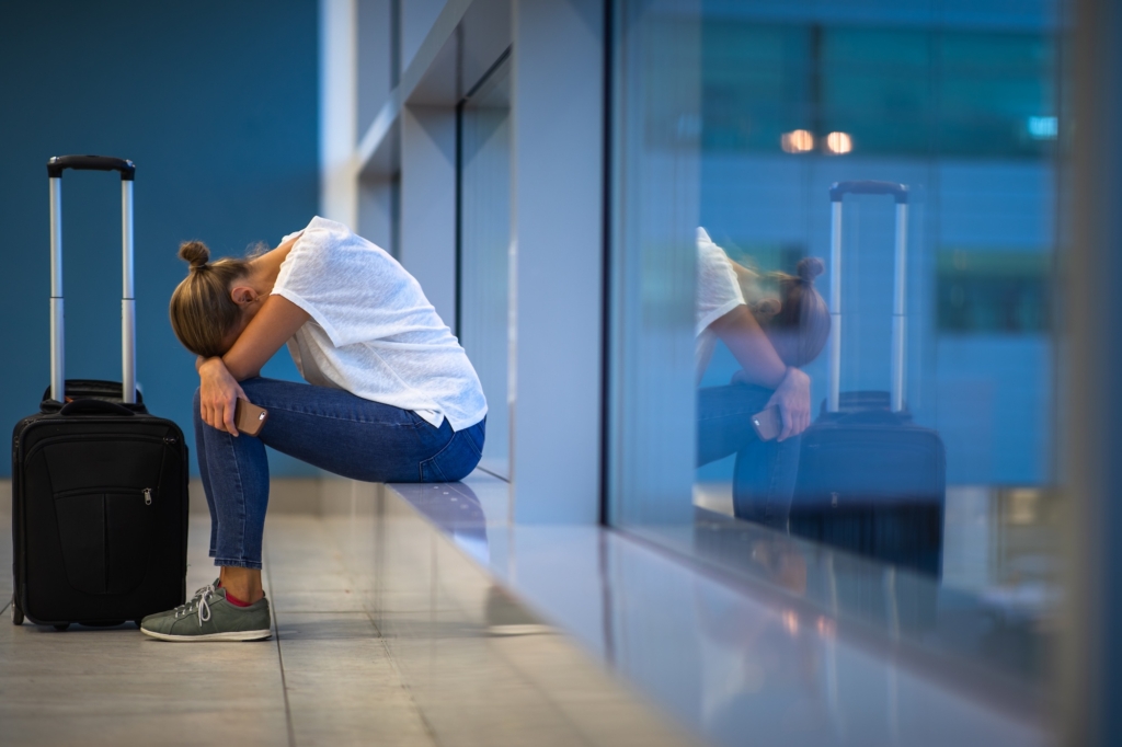 Exhausted female passenger waiting for her re-scheduled/delayed flight with her luggage at an international airport