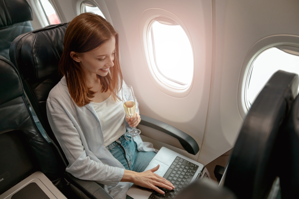 Smiling woman using laptop and drinking champagne in plane
