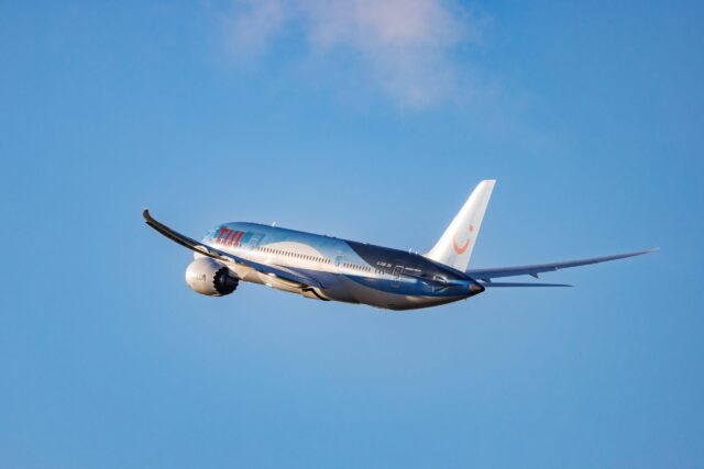 A Tui Boeing 787-8 flies against a bright blue sky