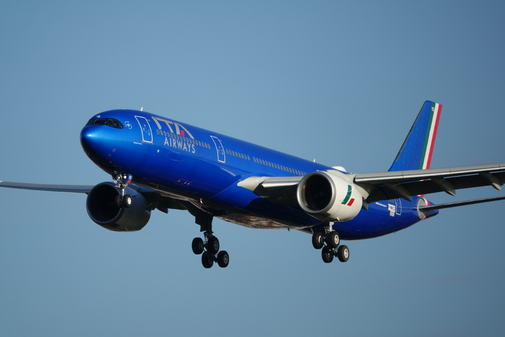 ITA Airways Airbus A330neo aircraft landing with a blue sky background.