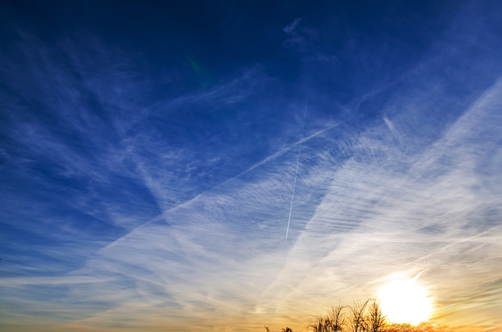 Vast blue sky filled with wispy clouds and airplane contrails during sunset. 
