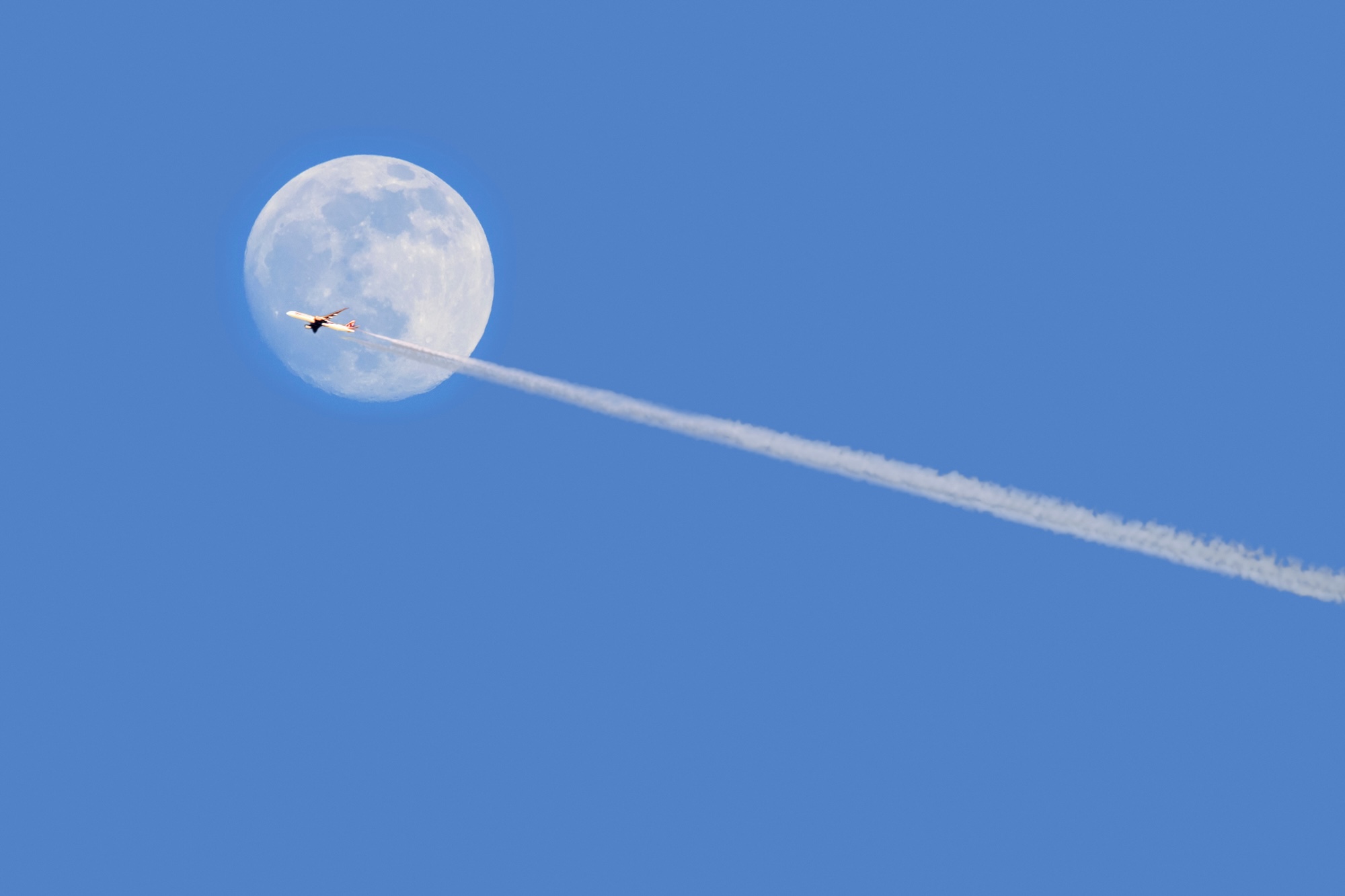 Commercial airliner / passenger plane flying in front of full moon at dusk showing contrails / condensation trails