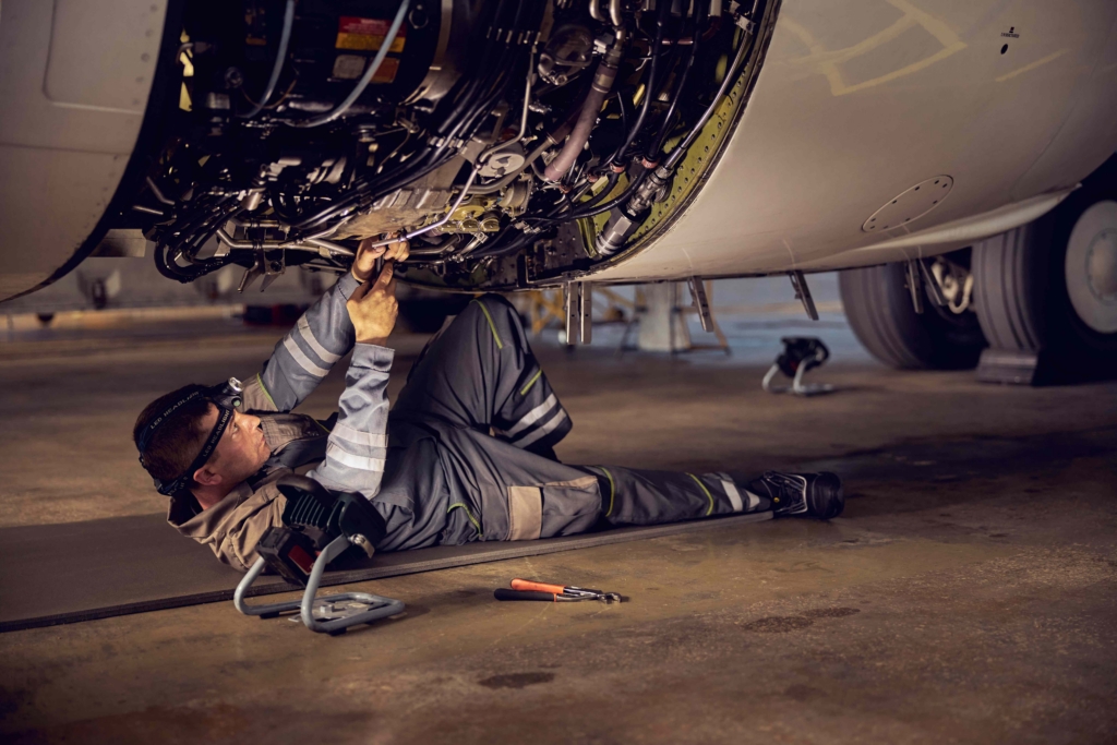 Side view portrait of airplane maintenance mechanic inspecting on aircraft engine in aviation hangar
