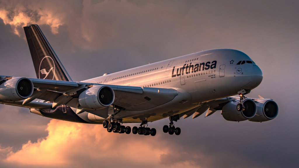 Lufthansa Airbus A380 aircraft landing at sunset with clouds in the background.