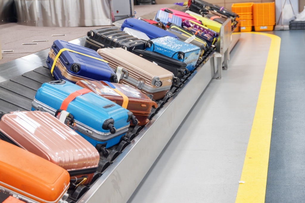 Bright suitcases and bags on luggage conveyor belt at arrival area of passenger terminal in airport. Baggage carousel.