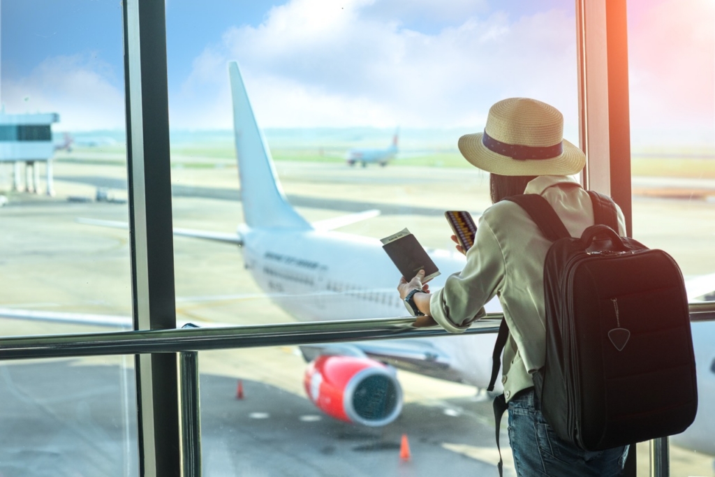 Woman passenger looking out of airport window with a phone