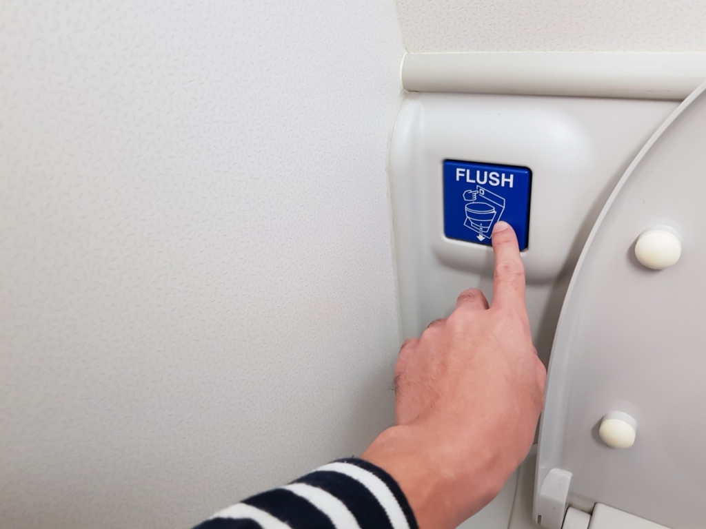 Hand pressing blue flush button sign at the air plane lavatory to clean after use. Interior toilet design to match with small space inside the aircraft.