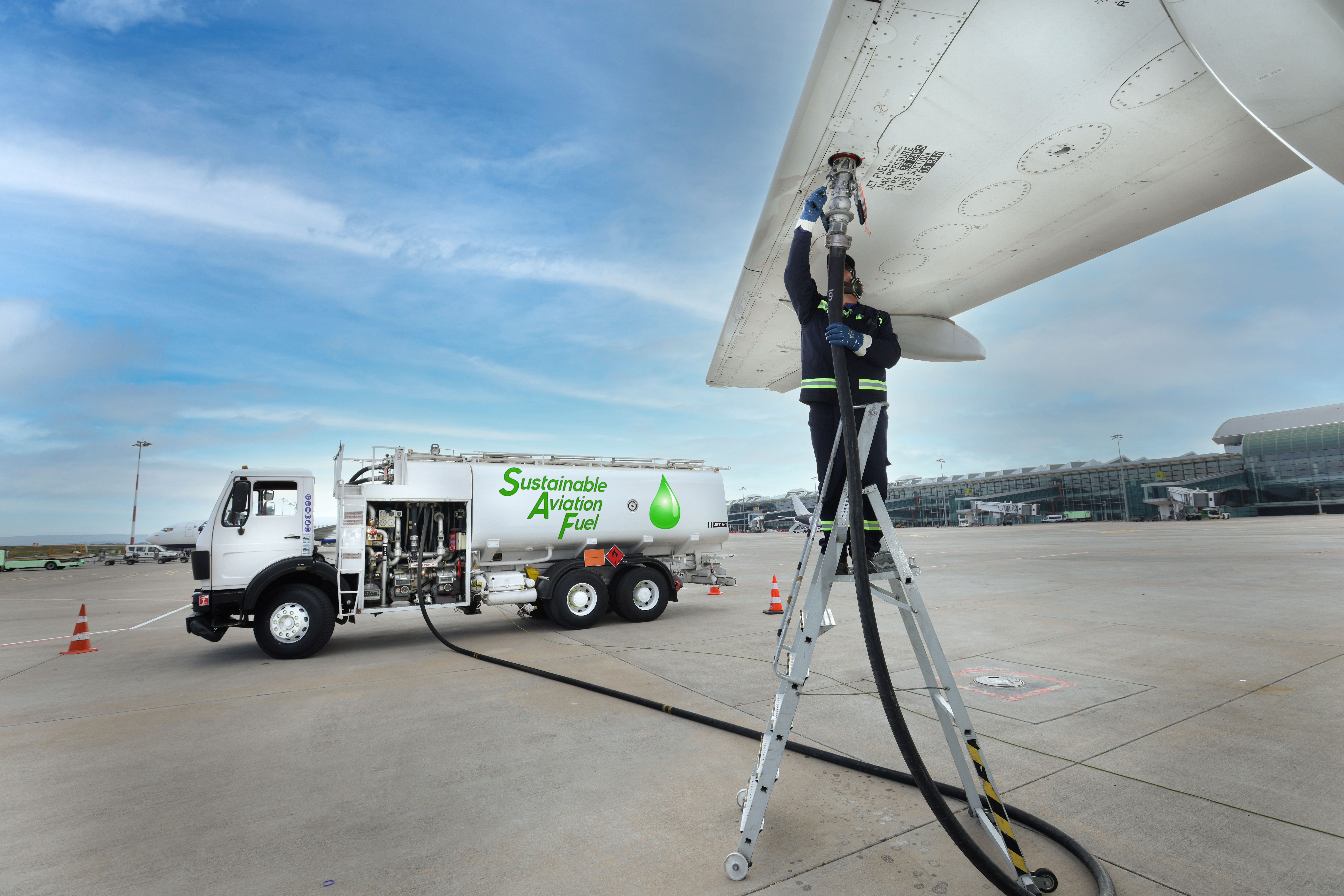 Technician is refueling aircraft with Sustainable Aviation Fuel (SAF) at the airport.