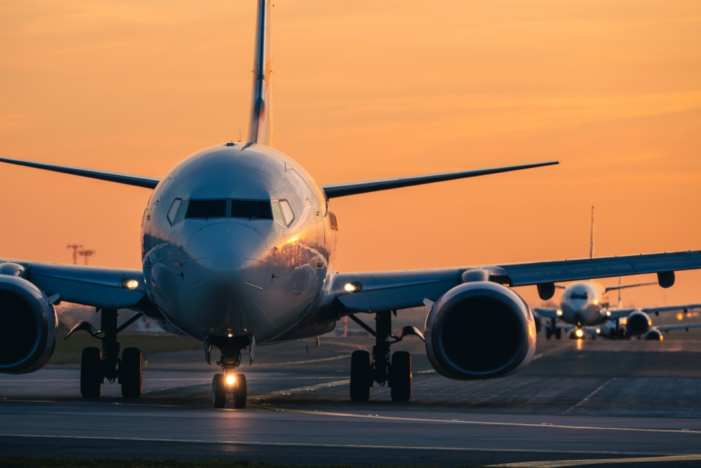 Line of passenger airplanes taxiing on airport runway for takeoff during peak hours at golden sunset dusk. Aviation, commercial flight congestion, air transport and travel industry concept.