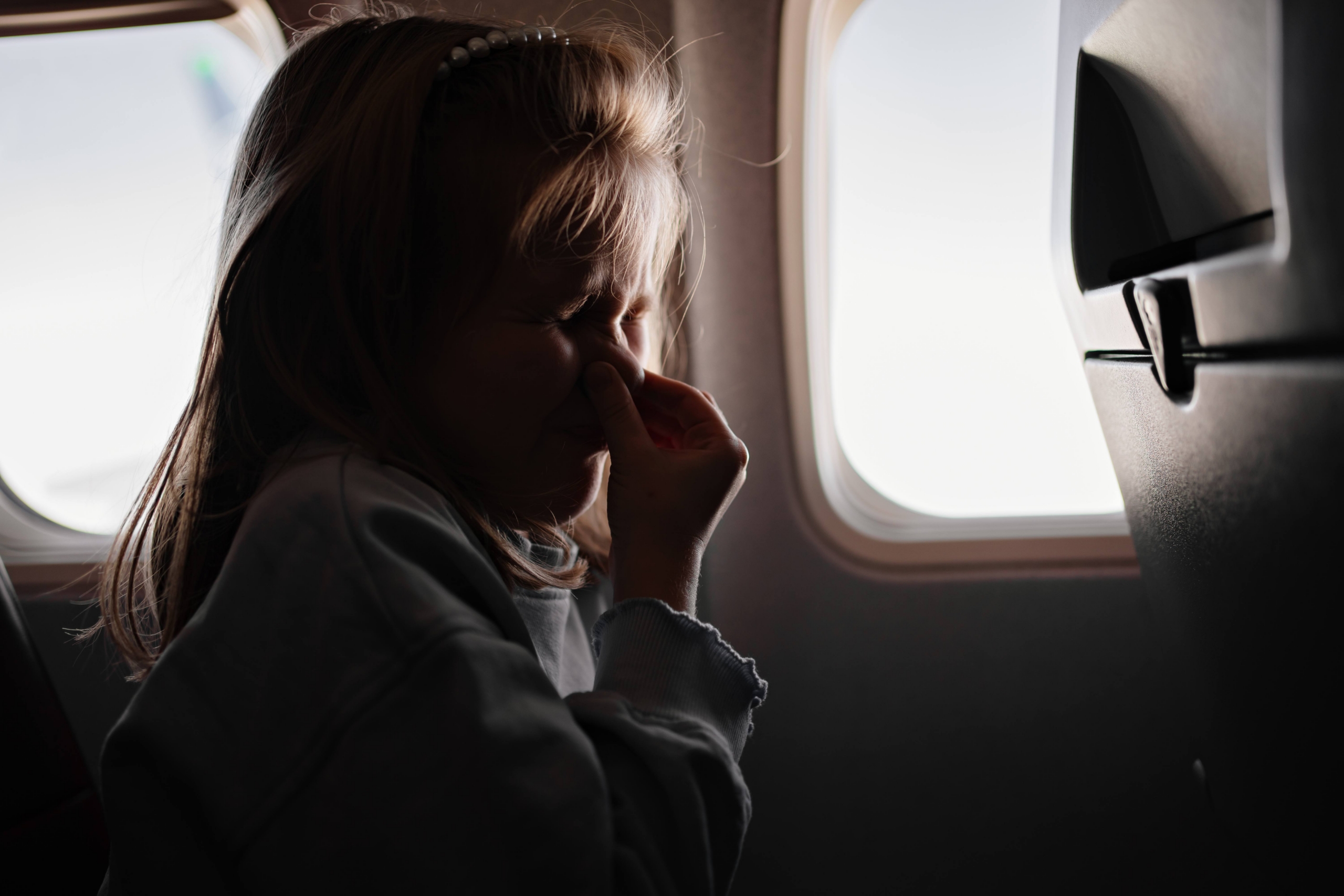 a little girl clamps the nose because of the unpleasant smell in an airplane seat by the window. flights with children in economy class. the smell of sweat, fumes and dirty feet from passengers